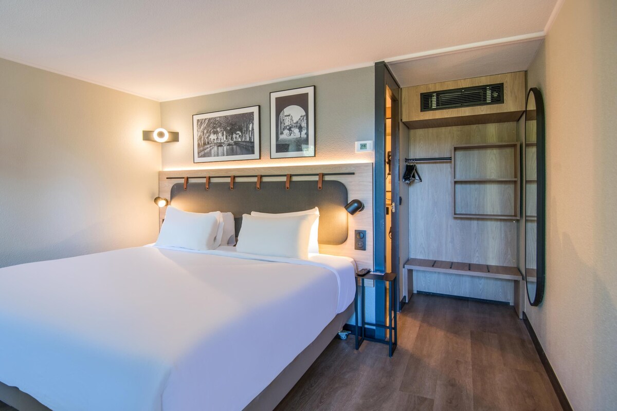 Un cuarto de hotel con una cama grande, un televisor de pantalla plana montado en la pared y un banco de madera en un rincón.