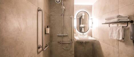 Un baño moderno con cabina de ducha, cabezal de ducha manual, dispensador de jabón manual, lavamanos con espejo y toallero con toallas dobladas.