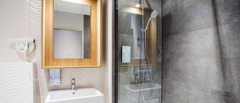 Un baño moderno con un lavabo blanco, un espejo y una ducha con mampara de vidrio.