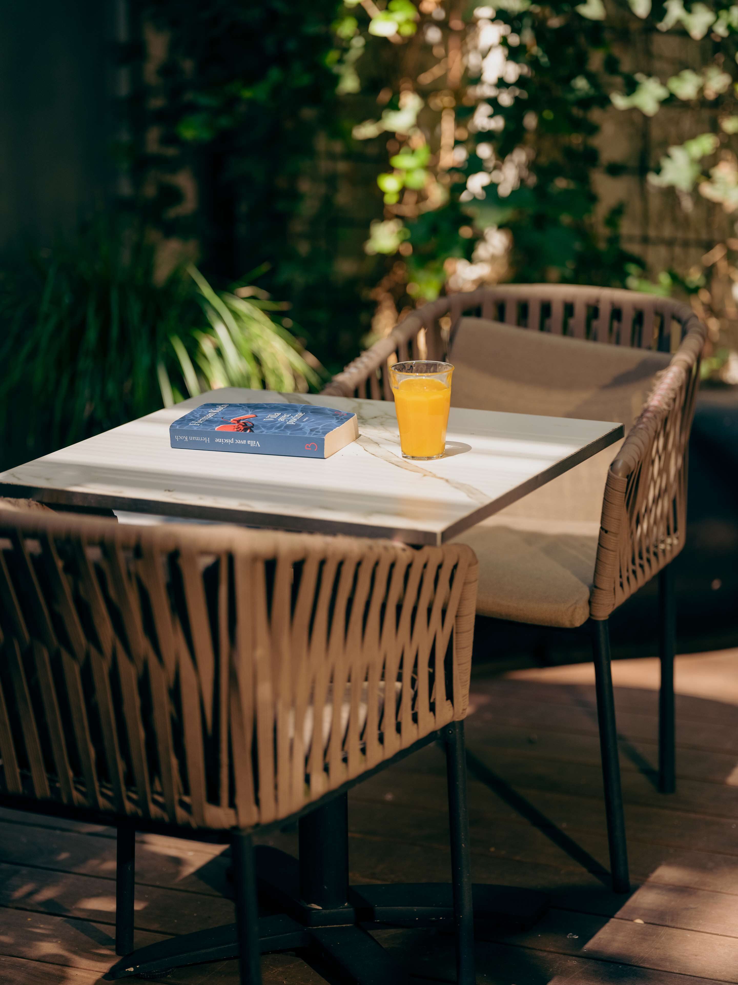 A table with a book and a glass of orange juice, surrounded by wicker chairs.