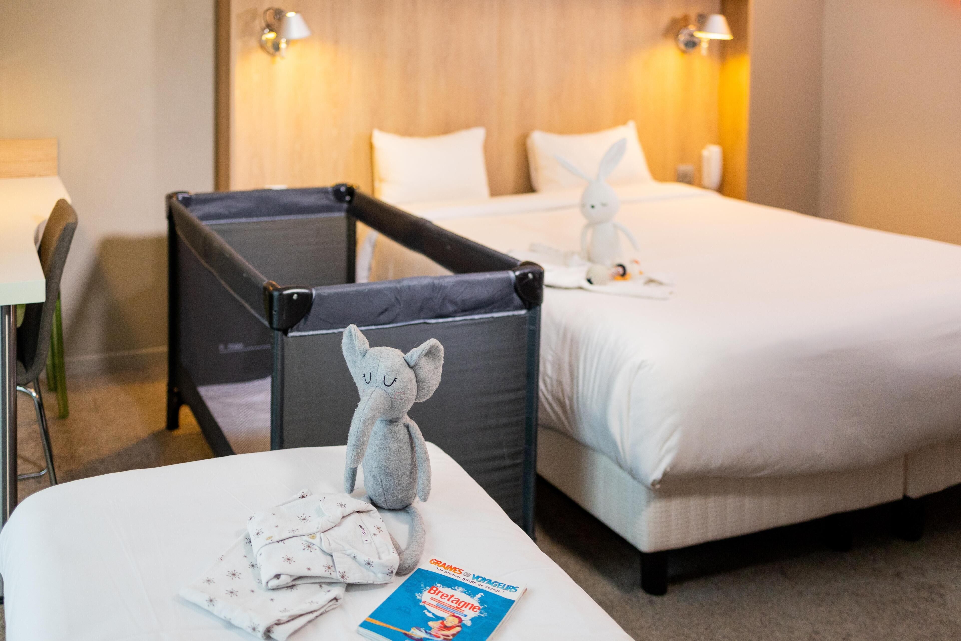 A hotel room with two beds, a chair, a stuffed toy, and a travel guide on the bed.