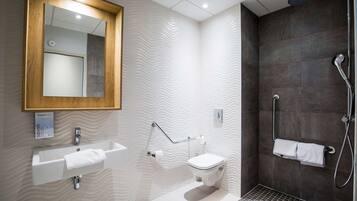 A modern bathroom with a wooden-framed mirror, a white sink, a toilet, and a walk-in shower with a dark tiled wall.