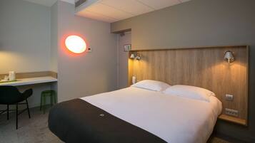 Una habitación de hotel con una cama grande, un escritorio con silla y una lámpara de pared.