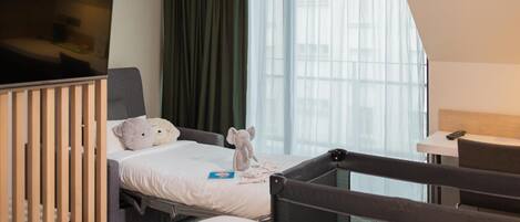 Una habitación de hotel con cama, una silla, televisor y ventana con cortinas.