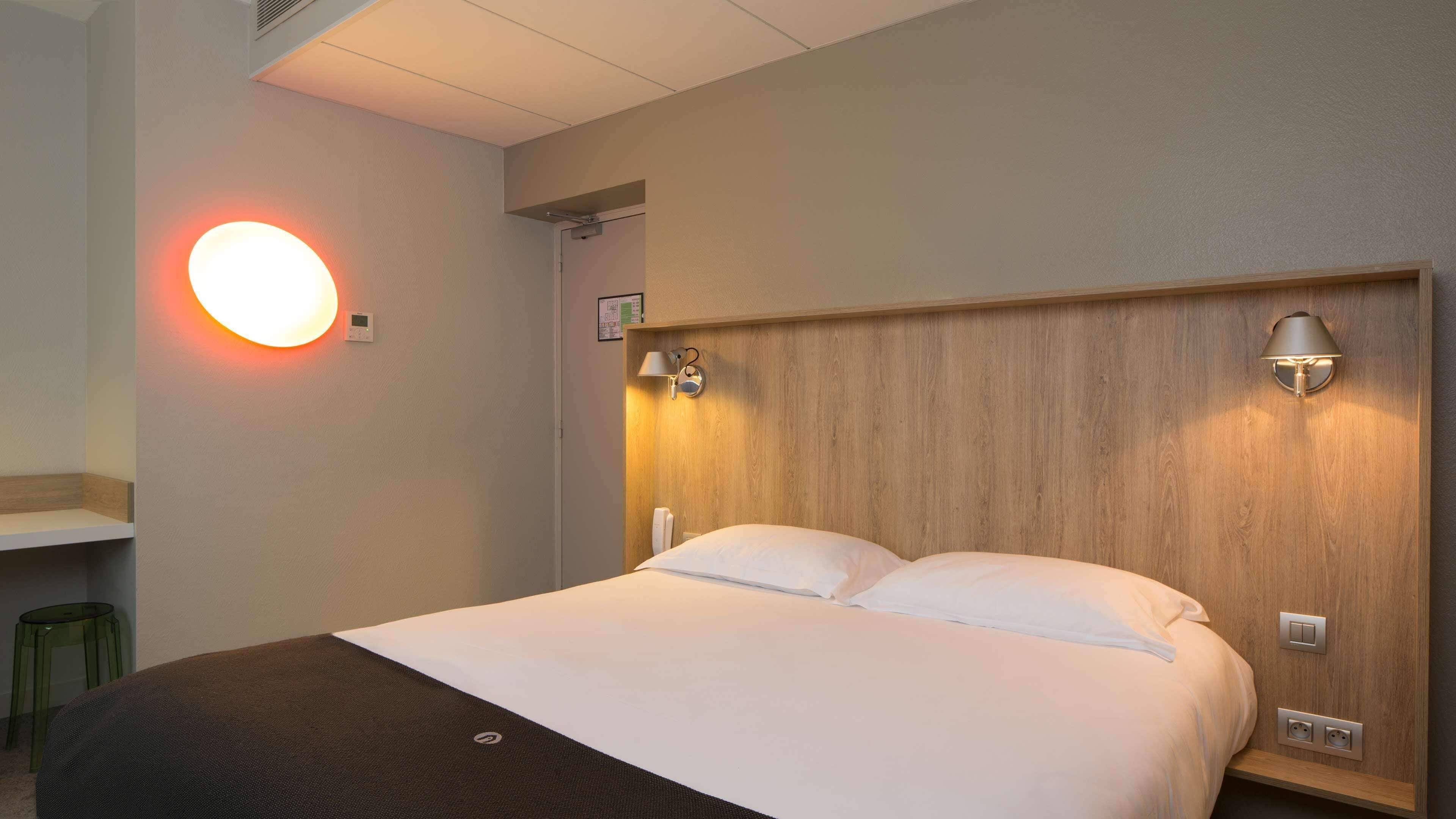 Una camera d'albergo con un letto, lampade ai comodini, una luce a parete e un tavolino con una sedia.