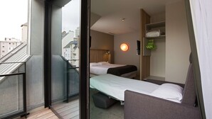 Habitación de hotel con balcón, cama, sofá y estante en la pared con objetos.