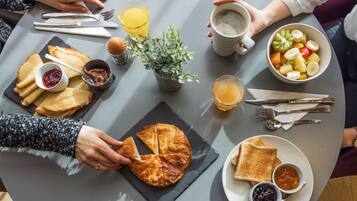 A round table with breakfast items including toast, jam, a croissant, fruit, and coffee.
