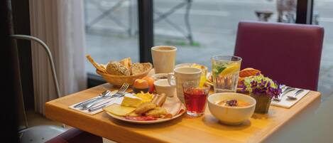 A breakfast table with various food items, cups, and a vase of flowers.