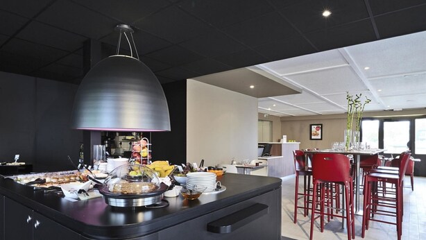 Un área de cocina moderna con una isla central, un comedor con sillas rojas y una barra.