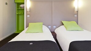 Habitación de hotel con dos camas, cada una con una almohada verde y cabecero negro. Hay un armario verde y un espejo en la pared.