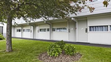 A row of white mobile homes with closed shutters, a small landscaped area with a tree, and a grassy lawn.