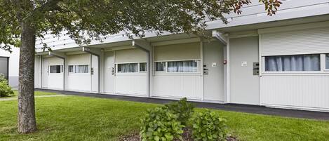 A row of white mobile homes with closed shutters, a small landscaped area with a tree, and a grassy lawn.