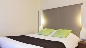 Een net opgemaakt bed met een zwart-wit dekbed, twee groene kussens en een nachtkastje met een lamp.