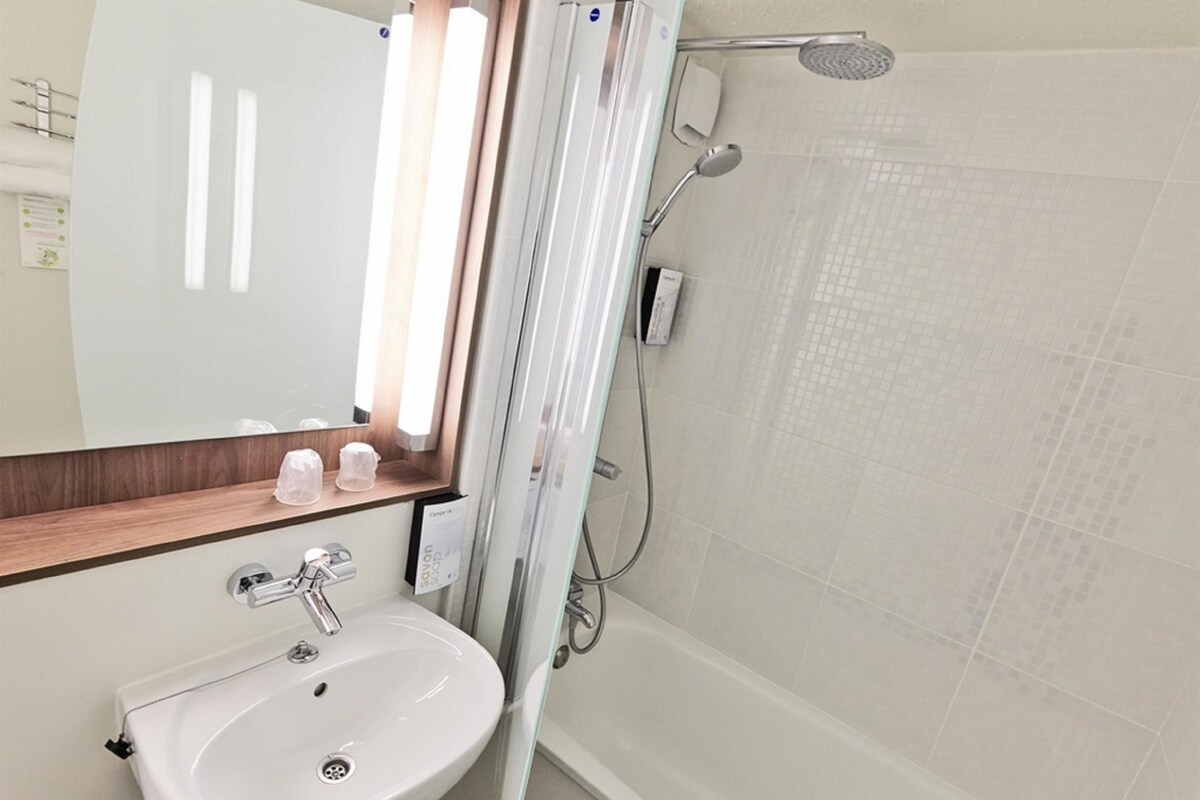 A bathroom with a white sink, mirror, and shower.
