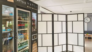 A vending machine with various beverages and snacks, a clock on the wall, and a wooden partition. - Kyriad Direct Strasbourg Ouest - Zénith (Strasbourg)