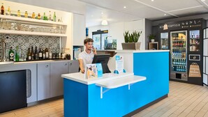 A modern bar area with a blue counter, shelves with bottles, and a refrigerator. - Kyriad Direct Strasbourg Ouest - Zénith (Strasbourg)