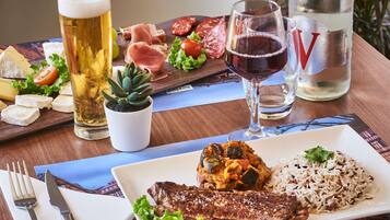 Een eettafel met diverse gerechten, waaronder steak, rijst en kaas, plus glazen bier en water.