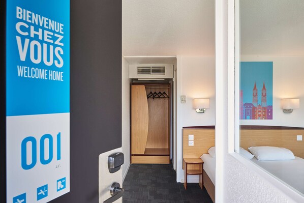 A hotel room with a bed, a desk, and a wardrobe. There is a sign on the wall that says "Bienvenue Chez Vous Welcome Home." - Kyriad Direct Strasbourg Ouest - Zénith (Strasbourg)
