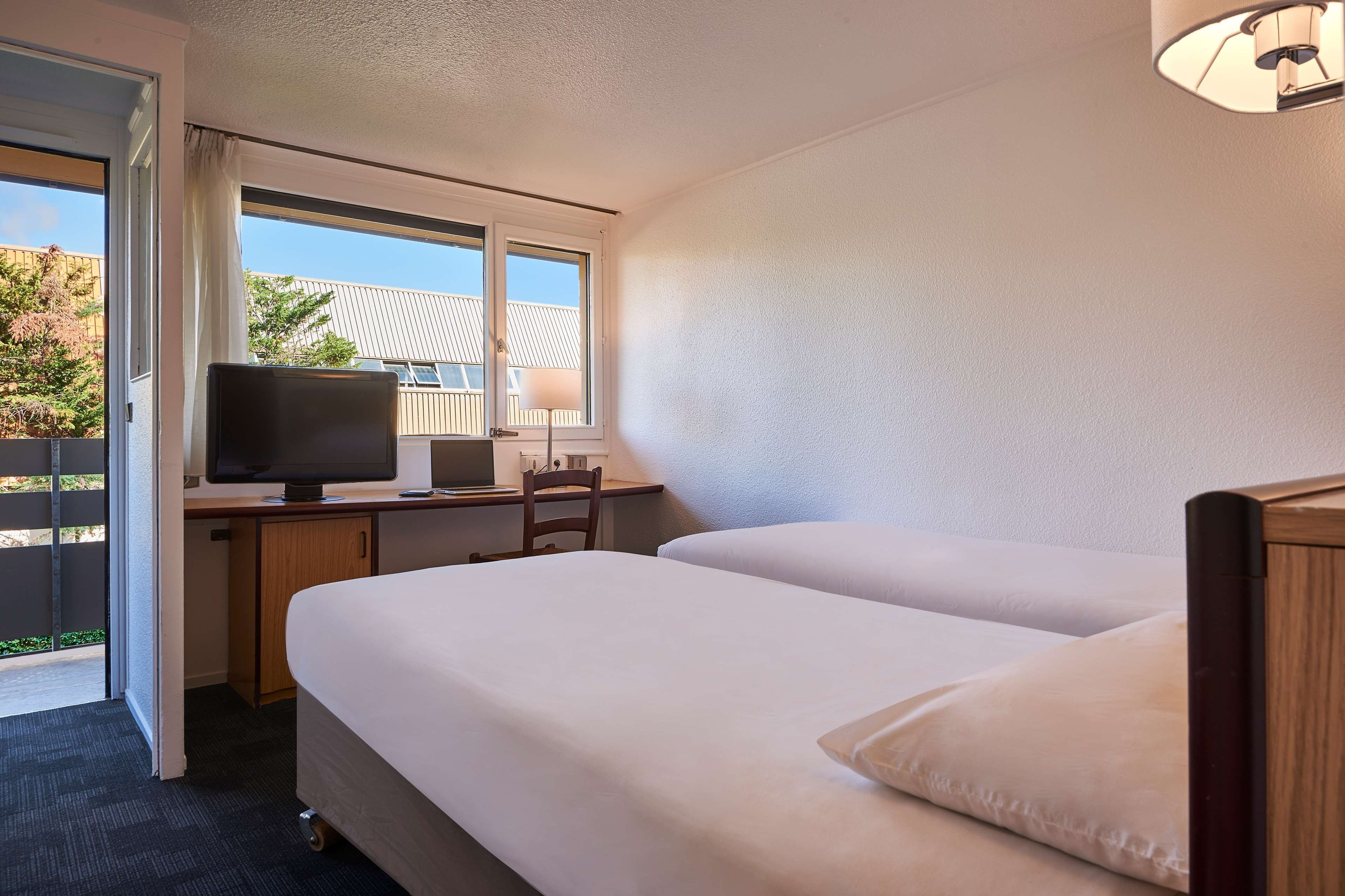A hotel room with a desk, computer, and two beds.