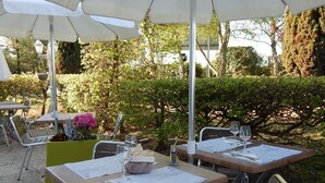 Un espace de restauration en plein air, avec des tables et des chaises, protégé par des parasols, et dont le décor est constitué d’une végétation luxuriante et d’arbres.