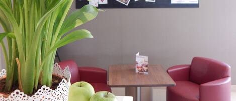 A room with a plant, red chairs, a table, and a bulletin board with photos and notes.