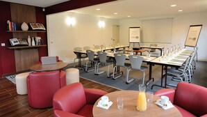 Une salle de conférence avec une longue table, des chaises rouges et un tableau blanc.