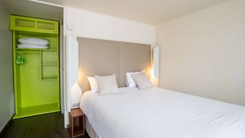 A hotel room with a large bed, a green wardrobe, and a bedside table.