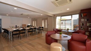 Una habitación amplia con una mesa grande y sillas, una mesita redonda con un control remoto y una estantería.