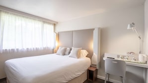 Una habitación de hotel con una cama grande, un escritorio con silla, una lámpara y una mesita de noche.