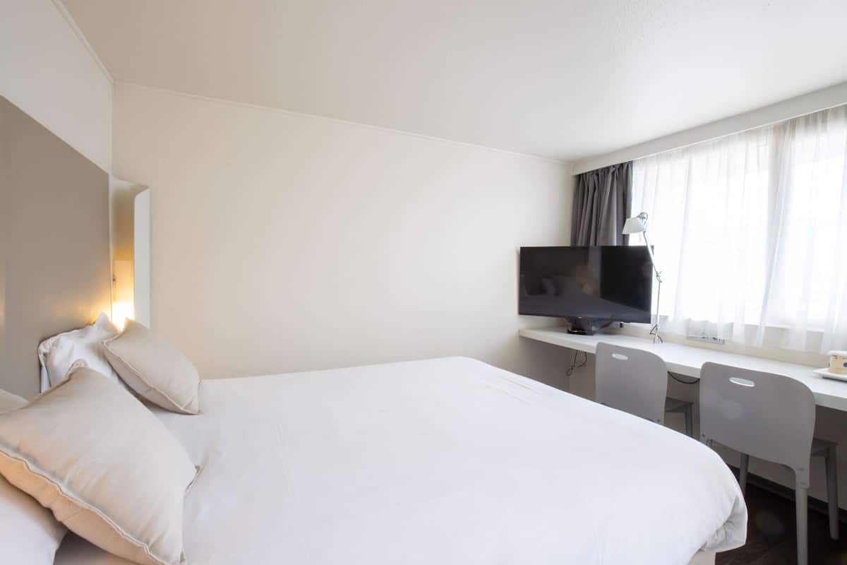 A hotel room with a large bed, a desk with a computer, and a TV.