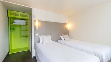 Una habitación de hotel con dos camas individuales, un armario verde y dos luces fijadas a la pared.