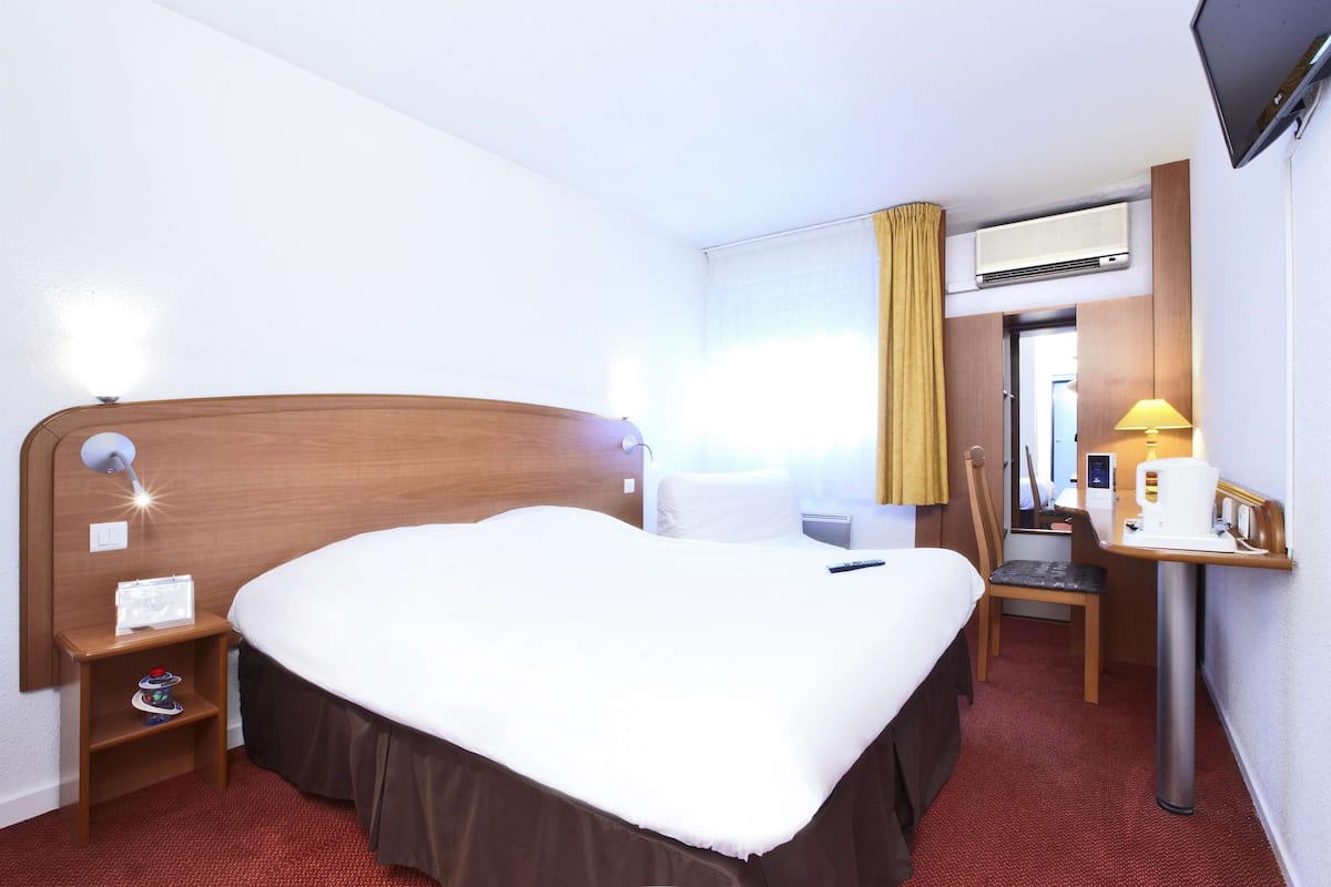 Une chambre d’hôtel avec un grand lit, un bureau avec une lampe, une chaise et un appareil de climatisation.