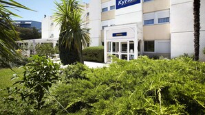 Een hotel genaamd 'Kyriad' met een moderne gevel, een duidelijke ingang en omliggend groen.