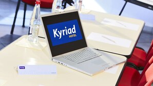 Een laptop op een tafel waarop 'Kyriad Hotel' staat, met een naambordje eronder.