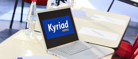 A laptop on a table displaying 'Kyriad Hotel' with a nameplate below it.