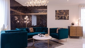 Ein modernes Wohnzimmer mit schwarzer Marmorwand, türkisfarbenen Sofas, einem weißen Couchtisch und einem goldenen Schrank.