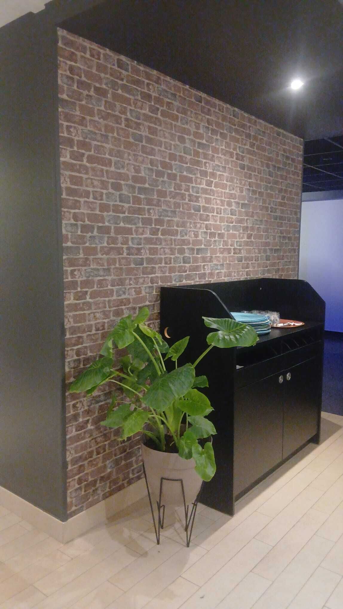 Une pièce moderne avec un mur en briques, un coin barbecue avec un gril noir et une plante en pot.
