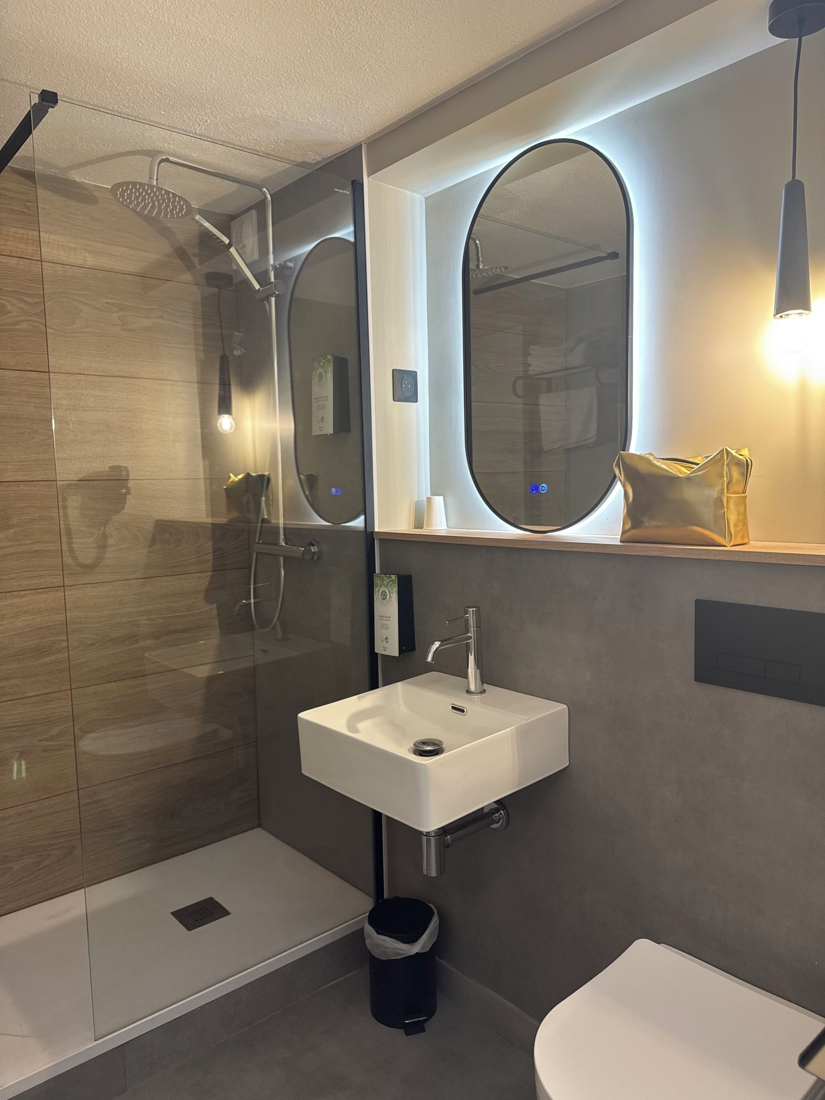 Ein modernes Badezimmer mit einer in Glas abgeschlossenen Dusche, einem weißen Waschbecken und einem großen Spiegel.