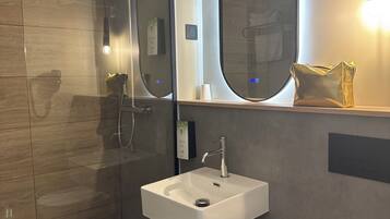 Ein modernes Badezimmer mit einer in Glas abgeschlossenen Dusche, einem weißen Waschbecken und einem großen Spiegel.