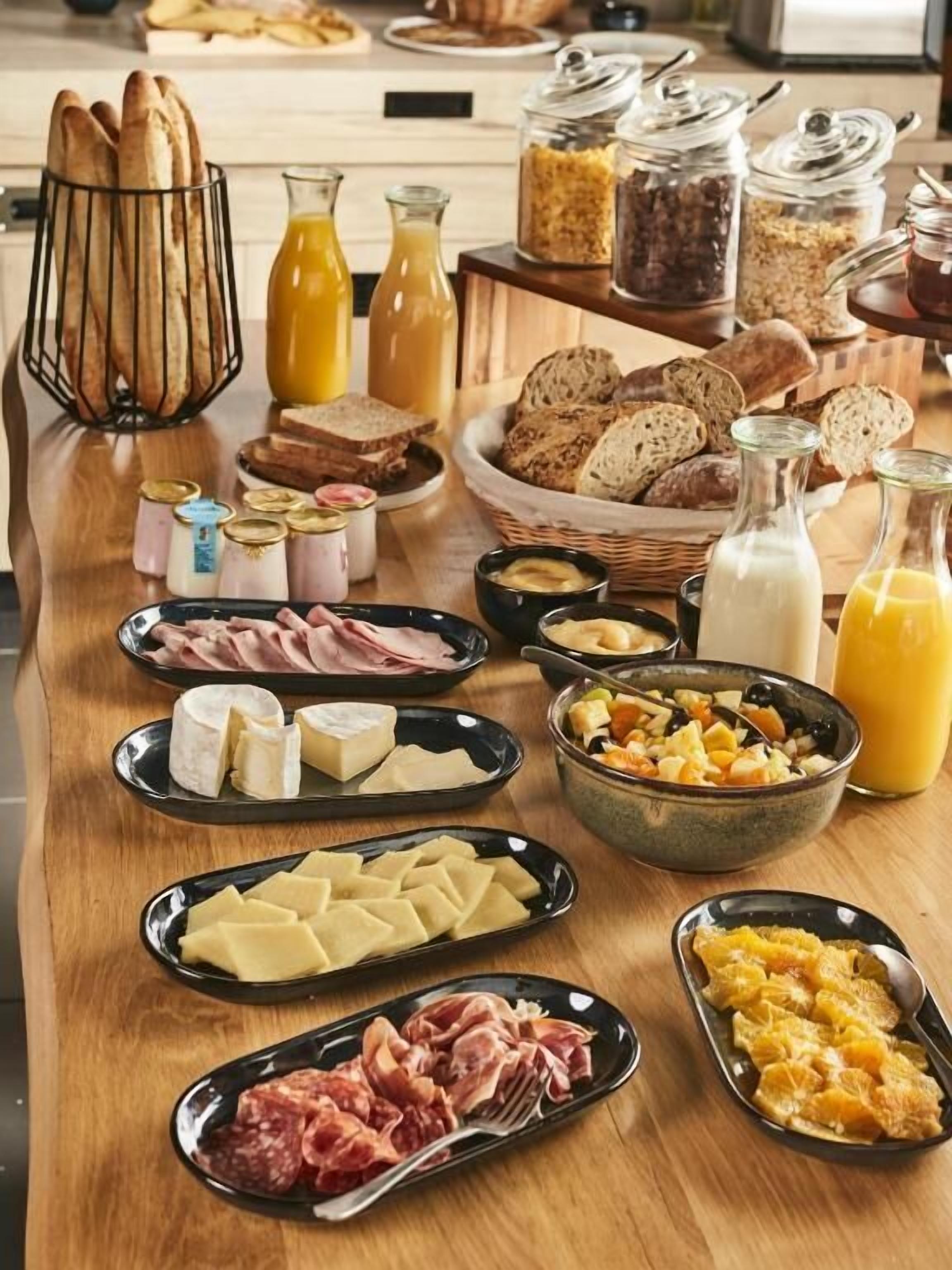 Un bufé de desayuno con varios quesos, carnes, panes y bebidas.