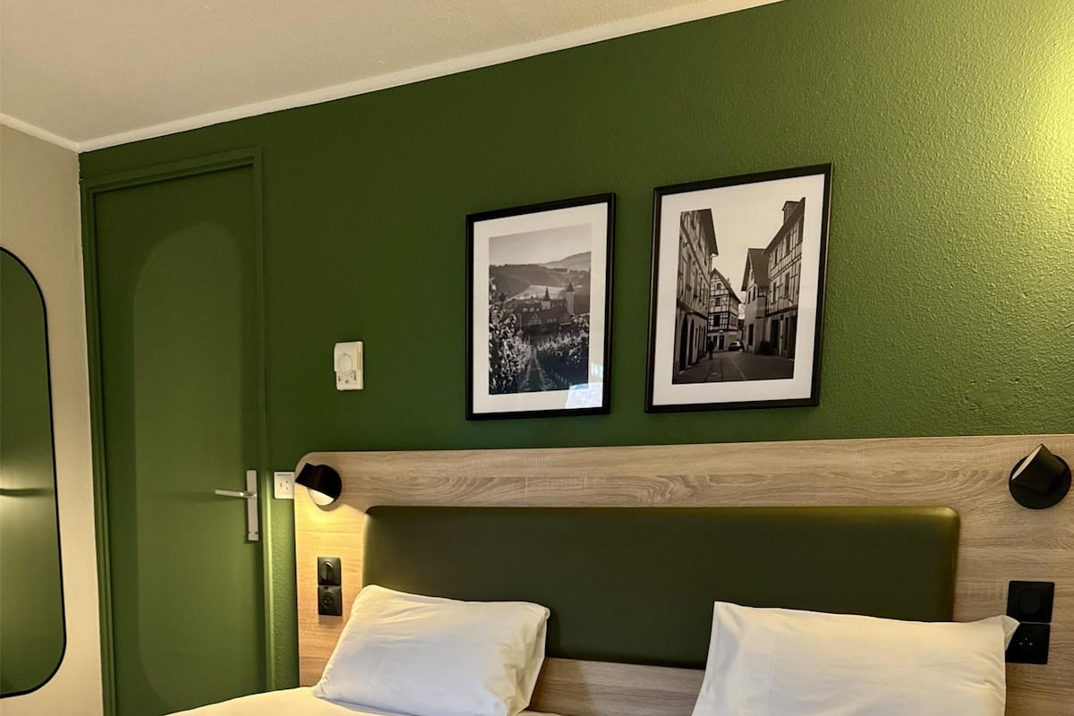 A hotel room with two beds, a green wall, and two black-and-white photographs.