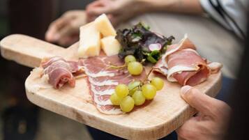 A wooden board with various food items including cheese, prosciutto, grapes, and greens.