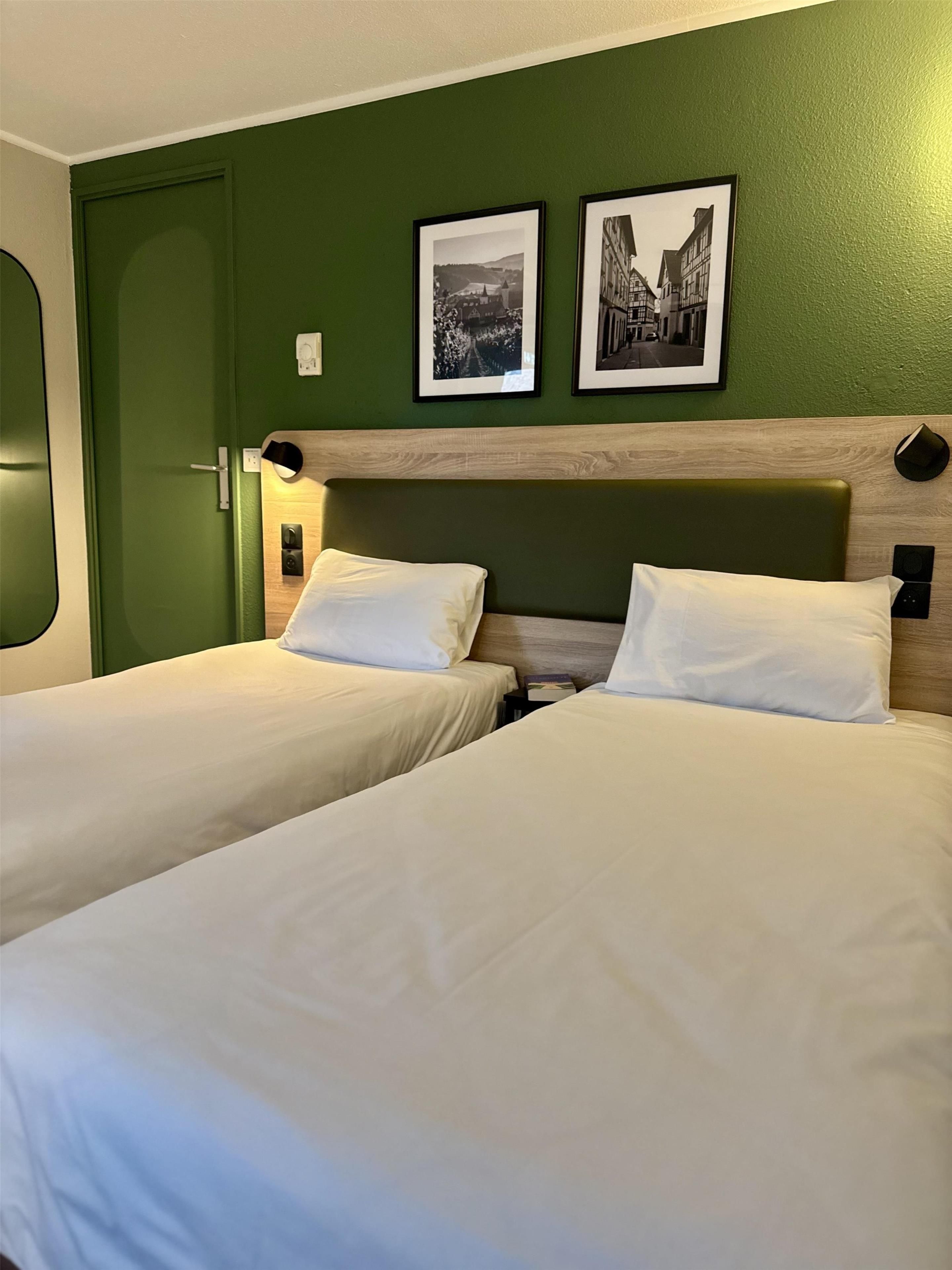 Et hotelværelse med to senge, en grøn væg og to sort-hvide fotografier.