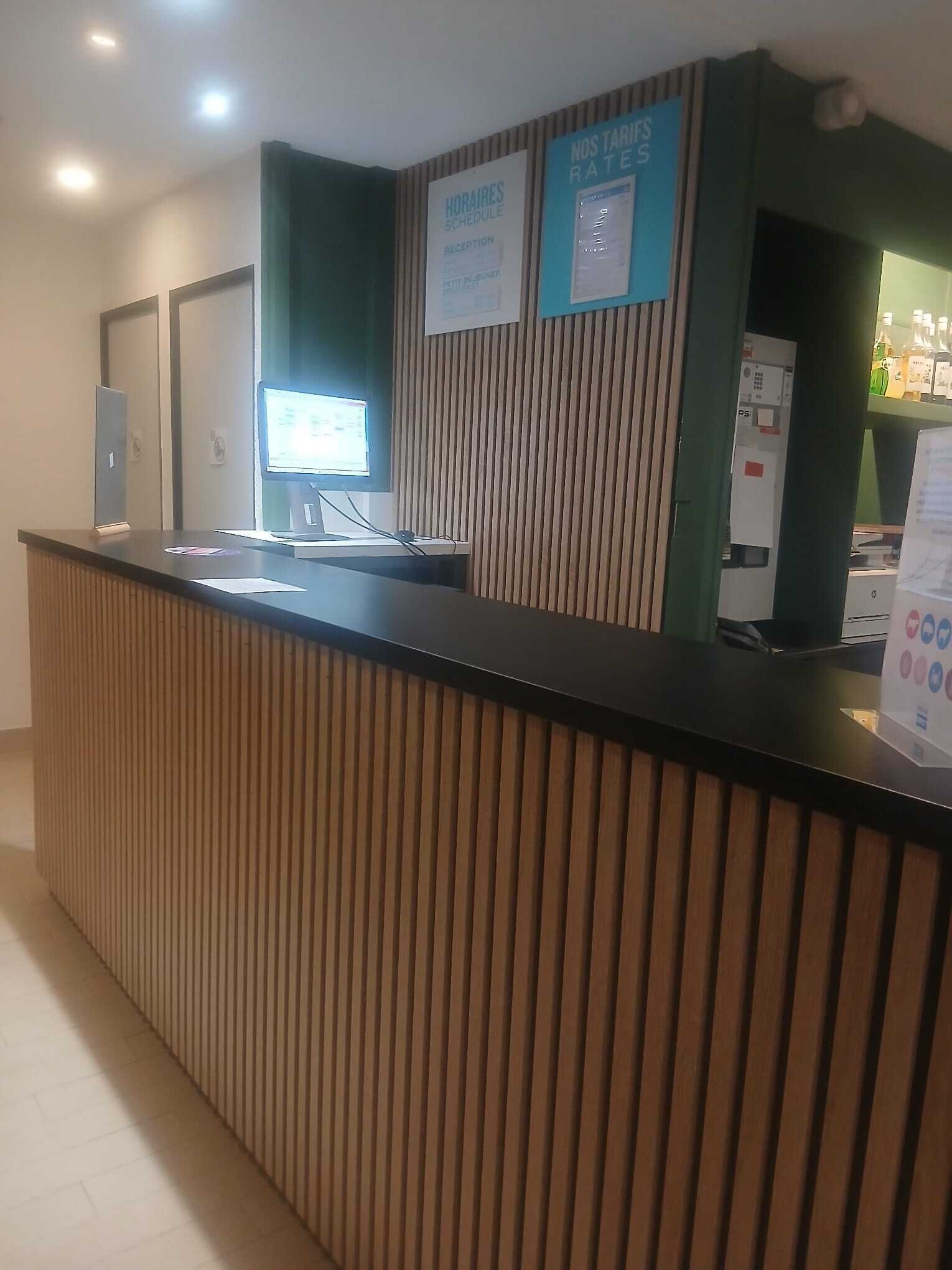 Tauleller de recepció amb un monitor d'ordinador, un quadre d'horaris i un panell d'informació sobre preus.