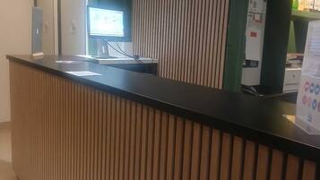 Tauleller de recepció amb un monitor d'ordinador, un quadre d'horaris i un panell d'informació sobre preus.