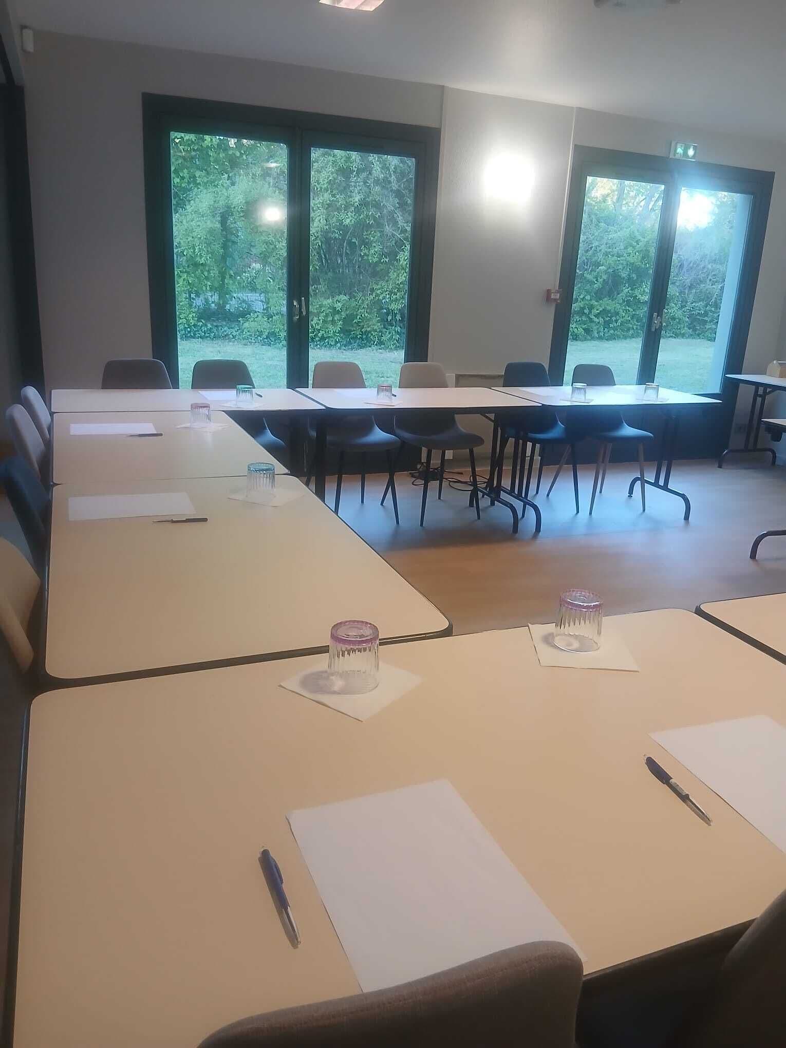 Un salón de conferencias con largas mesas, sillas y ventanas amplias que dan a zonas verdes.