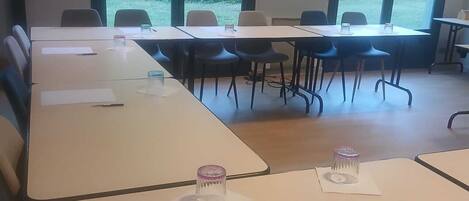 Un salón de conferencias con largas mesas, sillas y ventanas amplias que dan a zonas verdes.