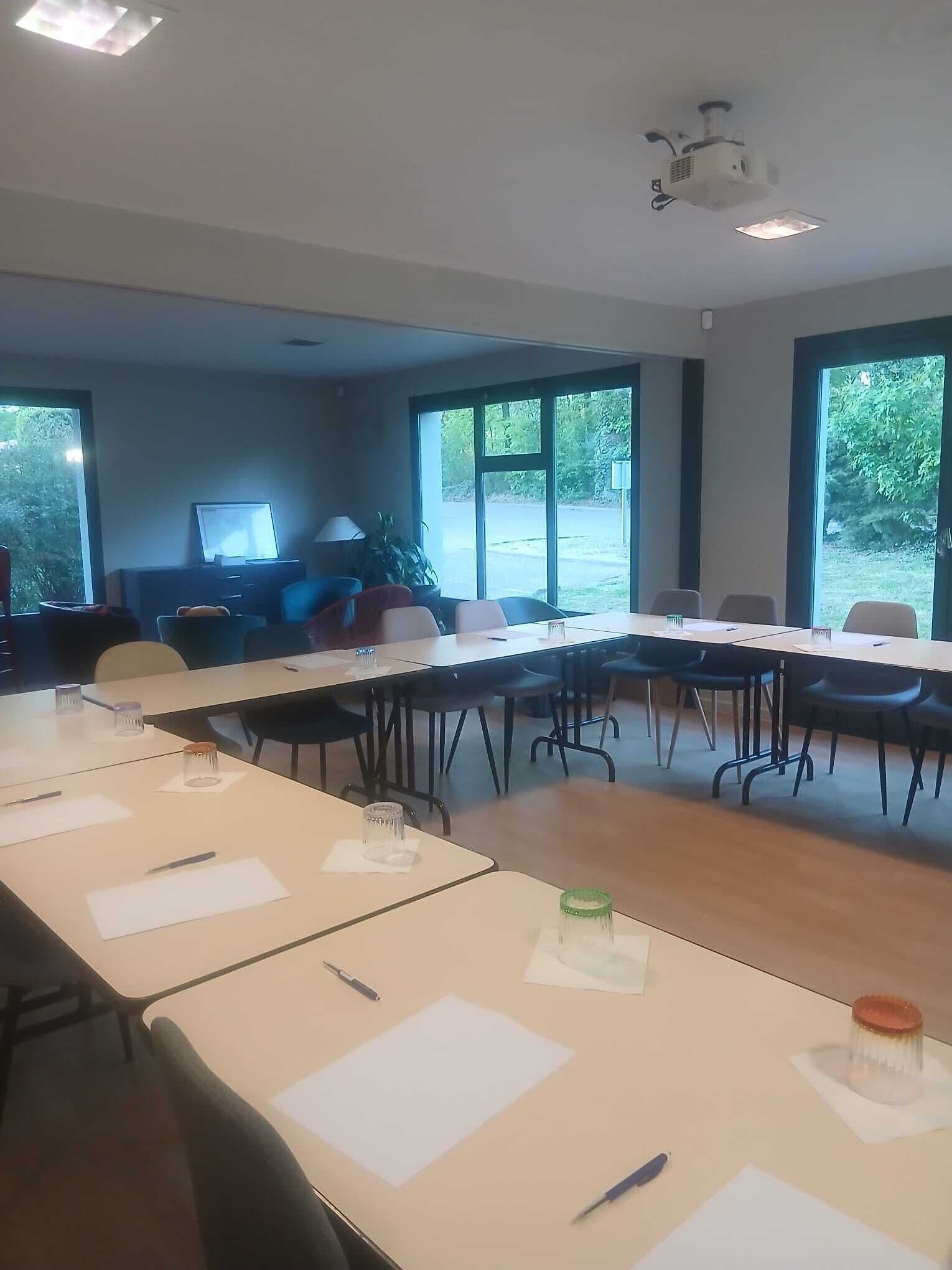 Ein Konferenzraum mit Tischen, Stühlen, einem Projektor und großen Fenstern.