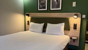 A neatly made bed in a room with green walls, two framed pictures, and a wooden headboard.
