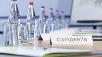 Ett skrivbord med flera glasflaskor, en skylt med texten ”Campanile Business” och en suddig datorskärm i bakgrunden.
